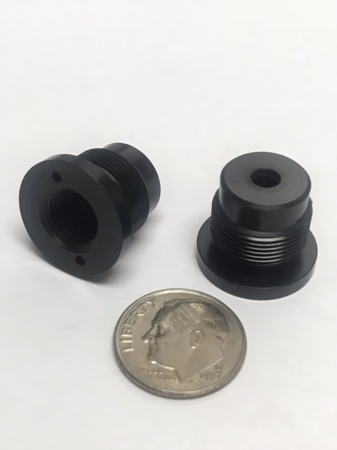 Two small black threaded cylindrical metal parts beside a 1997 US dime for size reference.