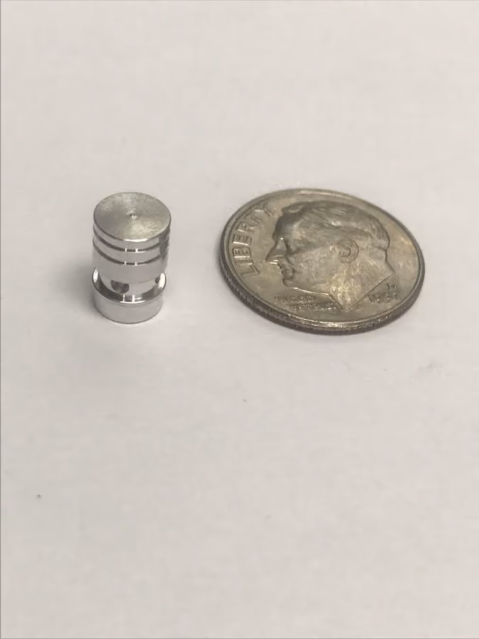 Small metallic cylindrical object next to a US dime on white surface for size comparison.