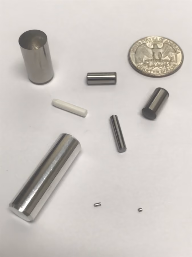 Various small cylindrical metal and one white ceramic pieces plus a quarter coin on a white surface.