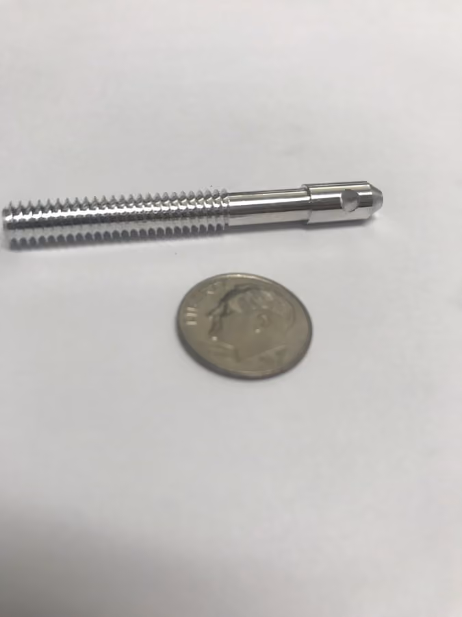 Metal threaded bolt next to a US dime coin on a white surface for size comparison.