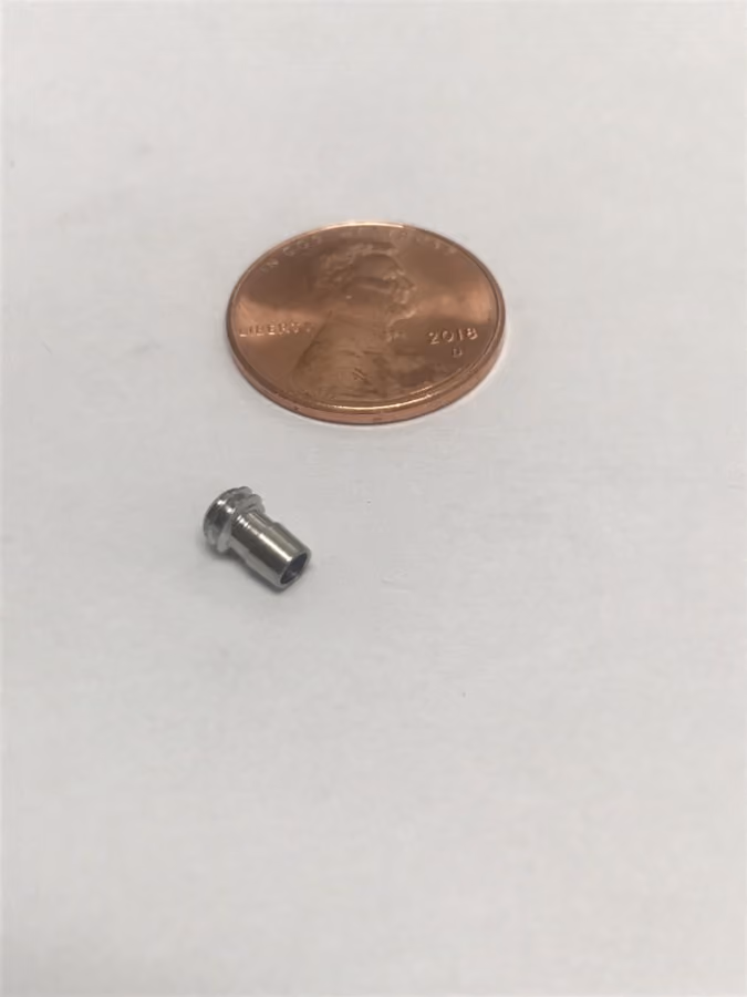 Small metal cylindrical object next to a 2018 US penny on a white surface.