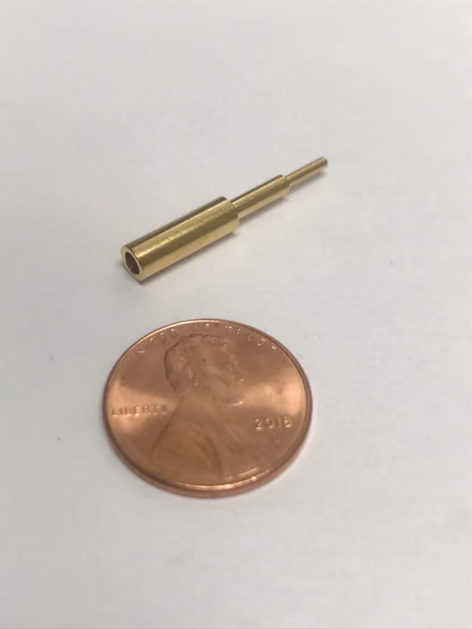 Small brass cylindrical object next to a 2018 US penny for size comparison.