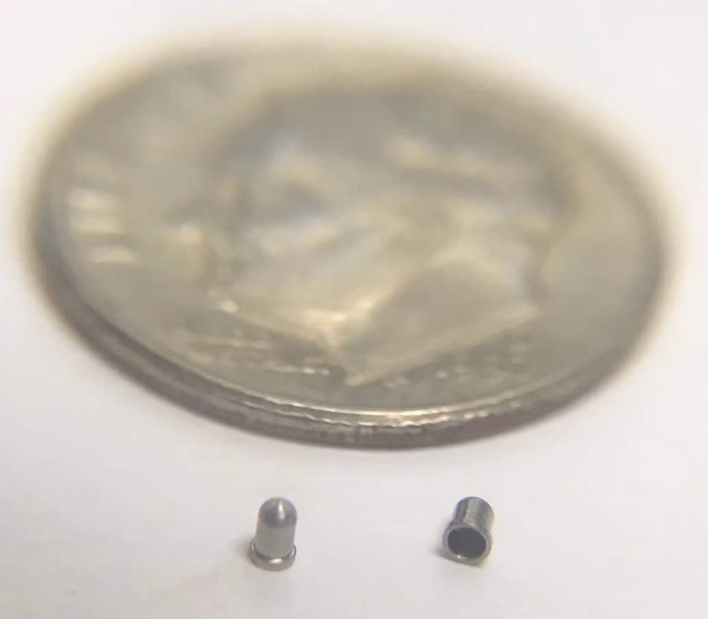 Two tiny metal cylindrical components next to a U.S. dime for size comparison.