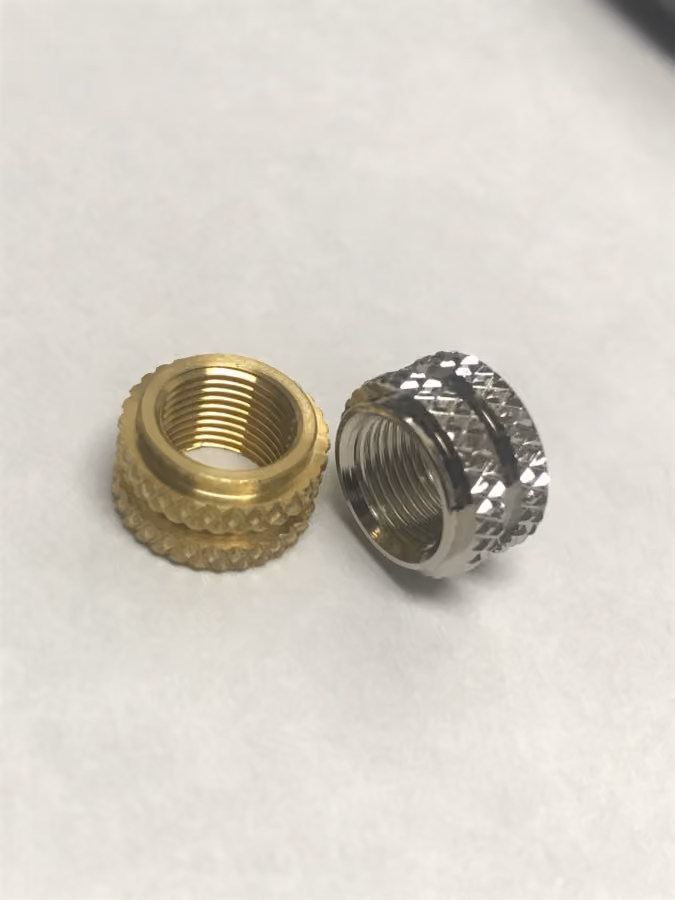One gold and one silver knurled threaded insert for hardware assembly on white surface.