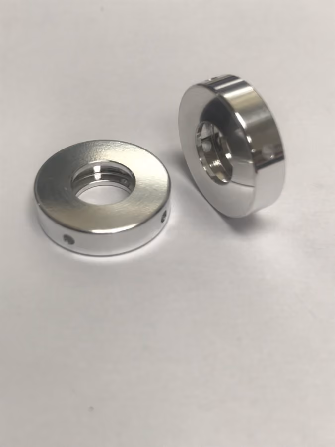 Two small shiny metal circular parts with holes, placed on a white surface.