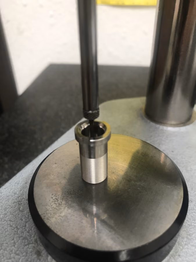 Metal cylindrical part held on a circular metallic base with a tool inserted into its center.