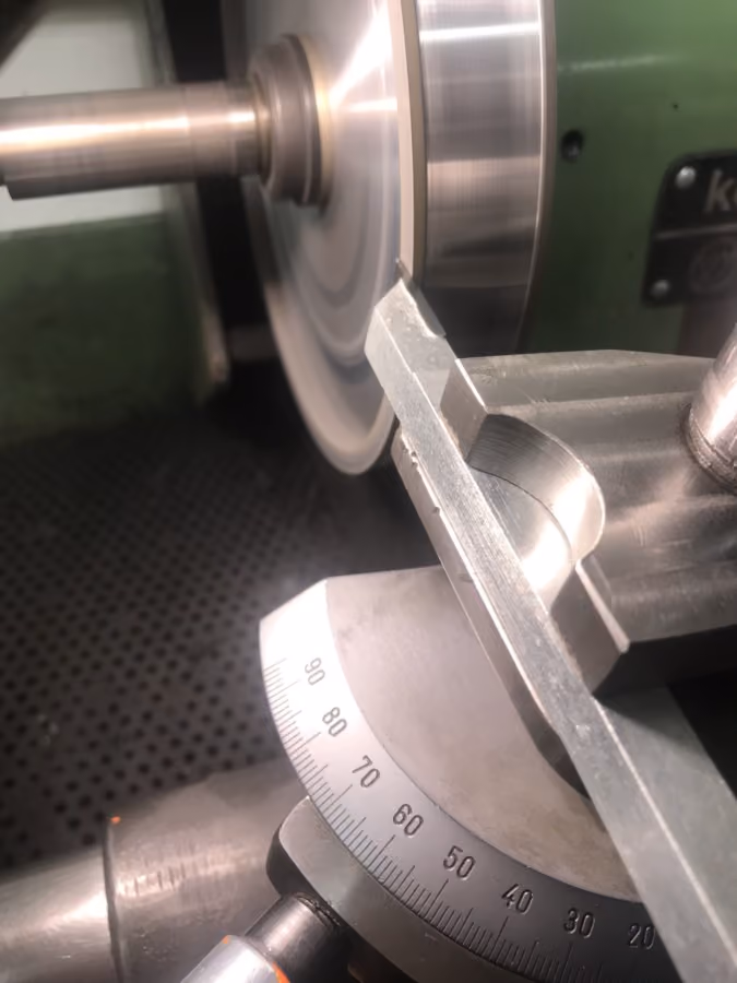 Close-up of a metal lathe machine cutting a cylindrical metal workpiece with angle dial visible.