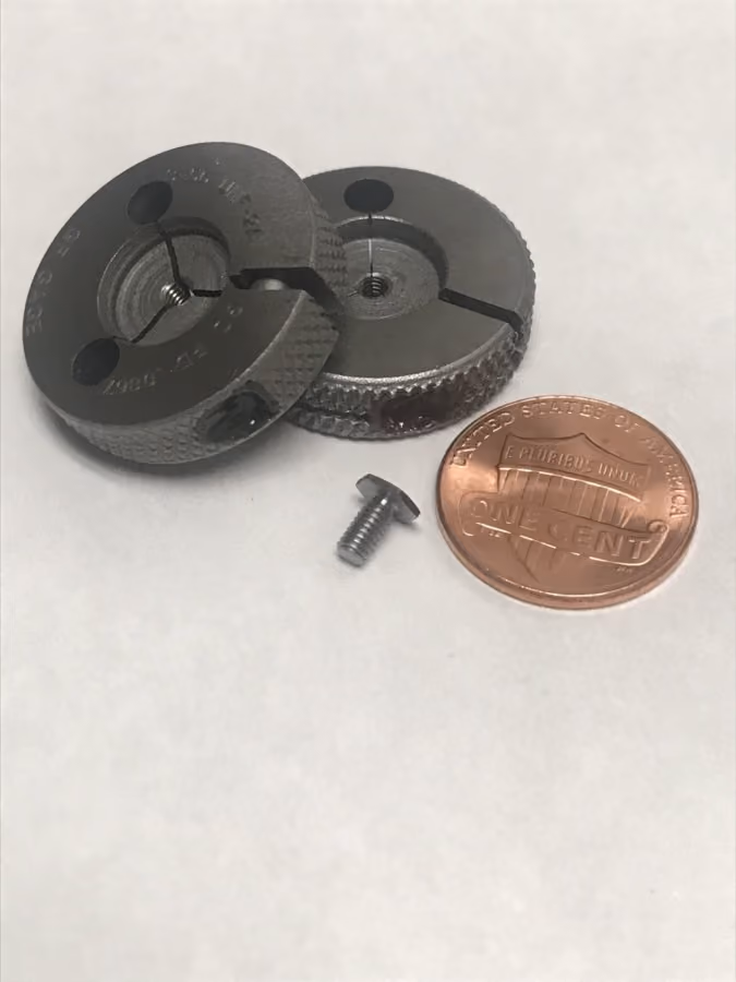 Two small metal round dies, one metal screw, and a US one-cent coin on a white surface.
