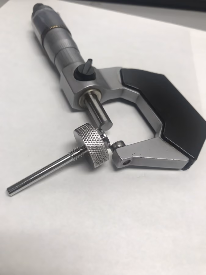 Close-up of a micrometer with a detached anvil spindle on a white surface.