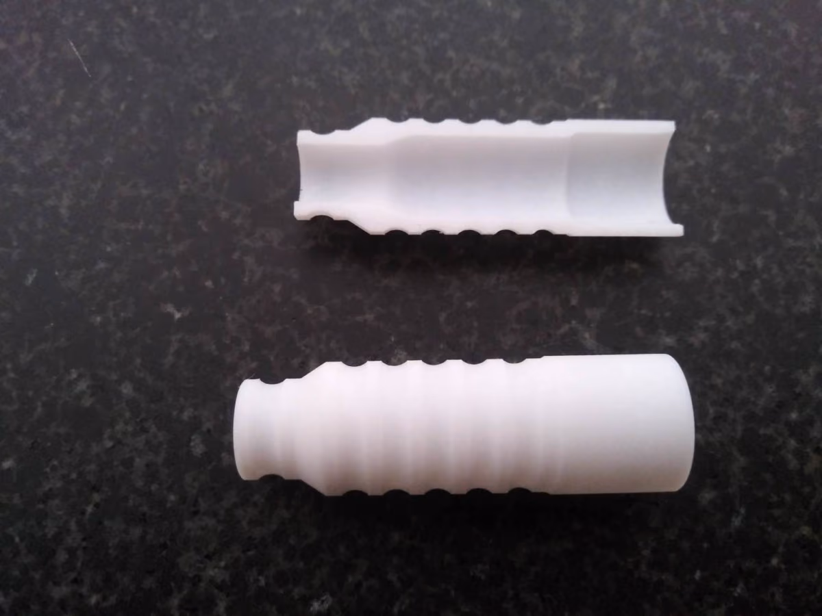 Two white plastic wall anchors on a dark textured surface, one whole and one cut in half.