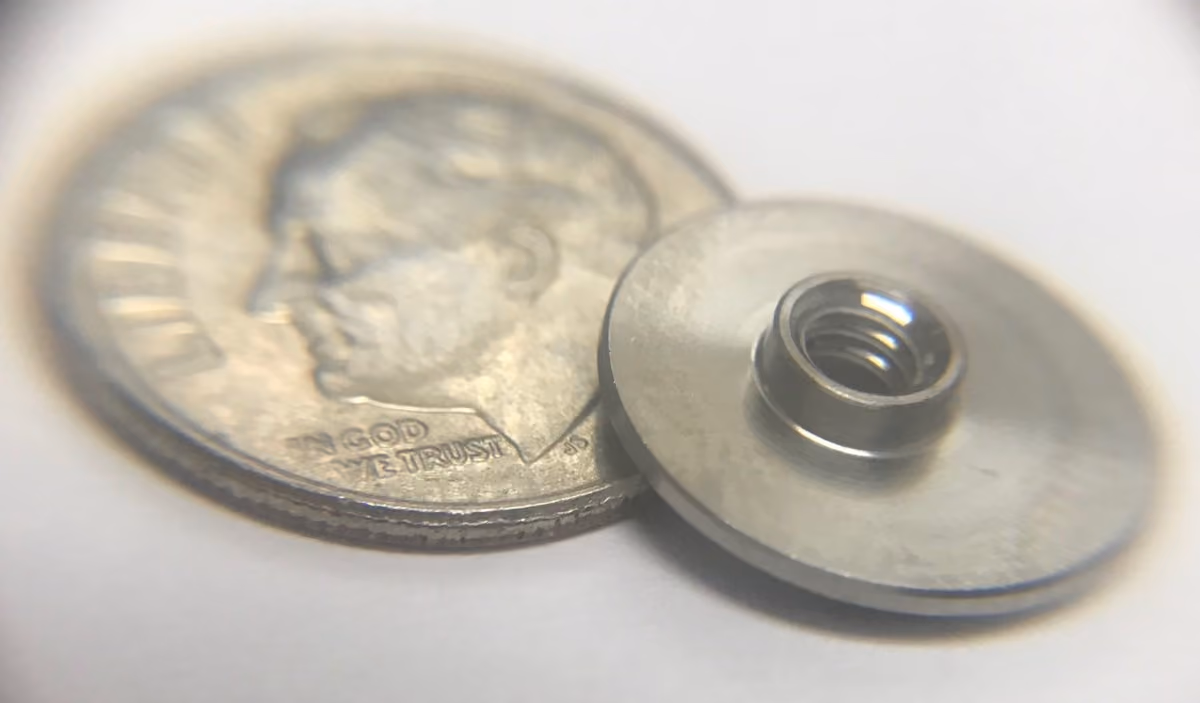 Close-up of U.S. dime coin beside a small metallic threaded circular component.
