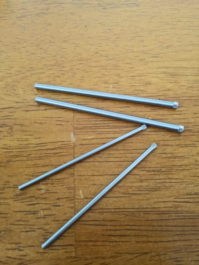 Four silver metal rods with knurled ends lying on a wooden surface.