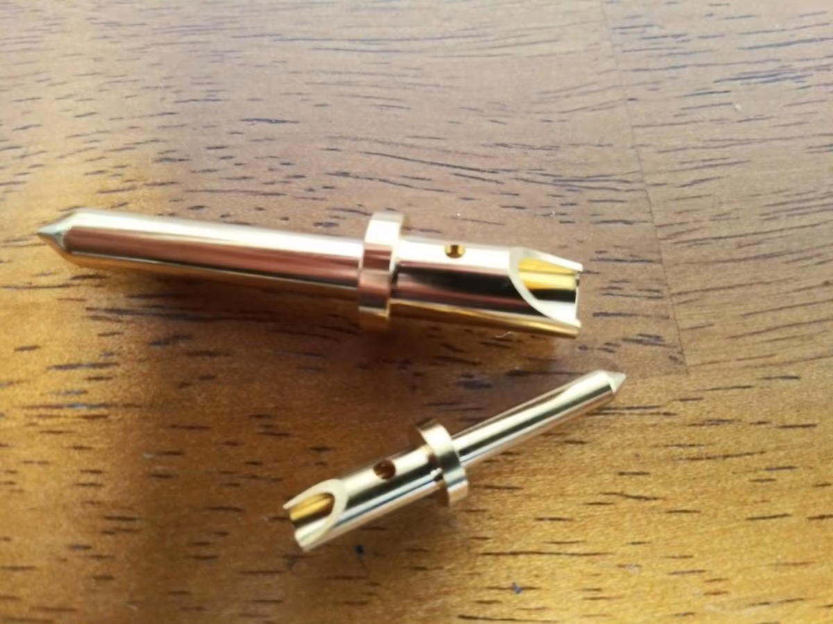Two gold-colored metal connectors with sharp tips lying on a wooden surface.