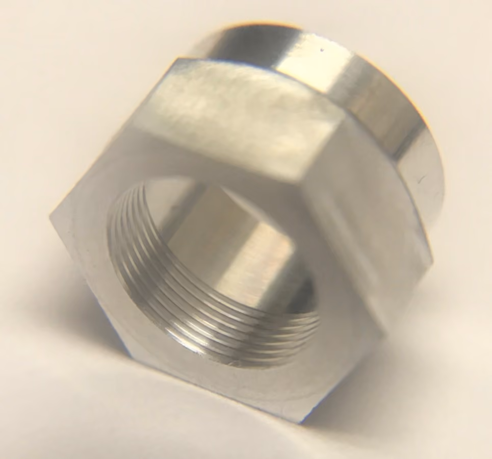 Close-up of a shiny metal hex nut with internal threading on a white background.