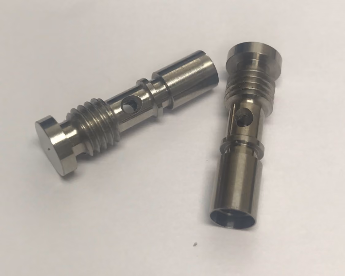 Two small shiny metal machine parts with cylindrical shapes and holes on a white surface.