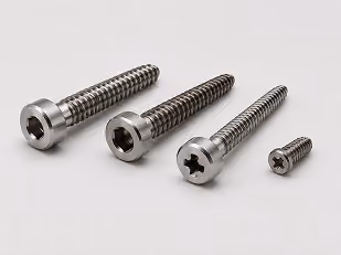 Four stainless steel screws of varying sizes on a light surface, arranged left to right from large to small.
