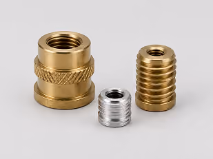 Three threaded brass and silver metal inserts of varying sizes on a white surface.
