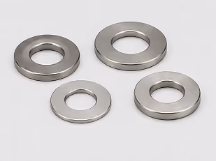 Four metallic flat washers of varying sizes arranged on a light gray surface.