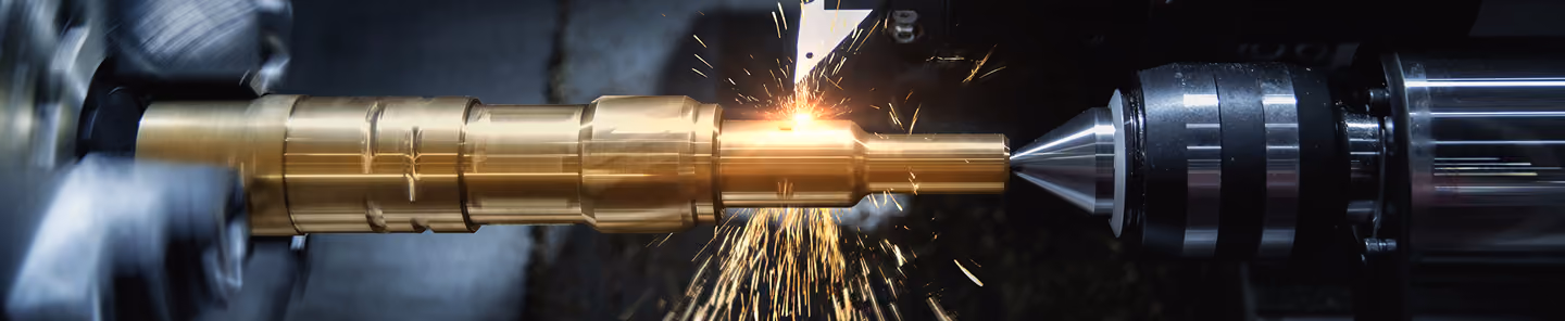Close-up of CNC lathe machining a brass shaft with sparks flying from cutting tool.