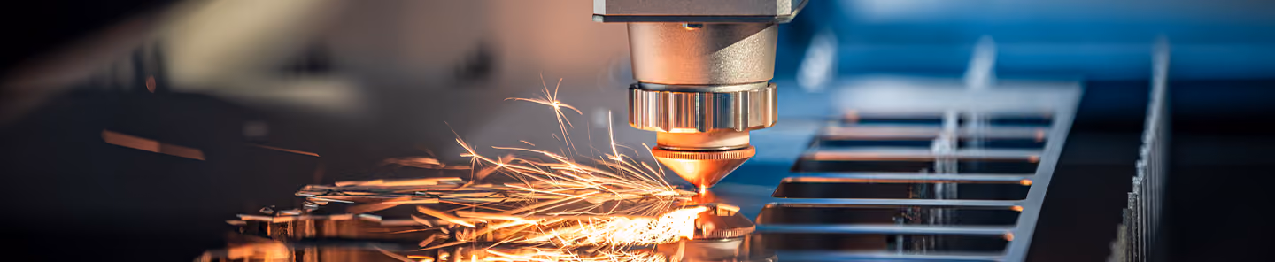 Close-up of a laser cutting metal sheets with bright sparks flying from the cutting nozzle.