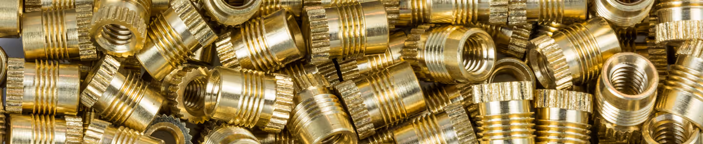 Close-up of many small cylindrical brass threaded inserts with knurled edges.