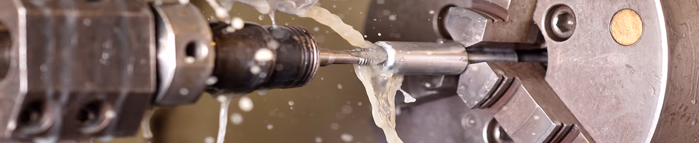 Close-up of a metal lathe machine cutting a cylindrical metal piece with coolant fluid spraying.