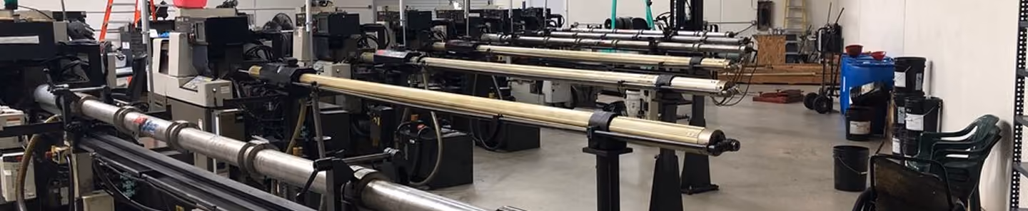 Industrial workshop with long horizontal metal pipes and machinery on a concrete floor.