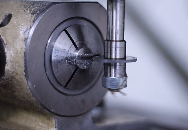 Close-up of a metal lathe machine cutting a cylindrical metal workpiece creating metal shavings.