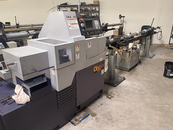 Cincom CNC lathe machine in an industrial workshop with concrete floor and tools in the background.