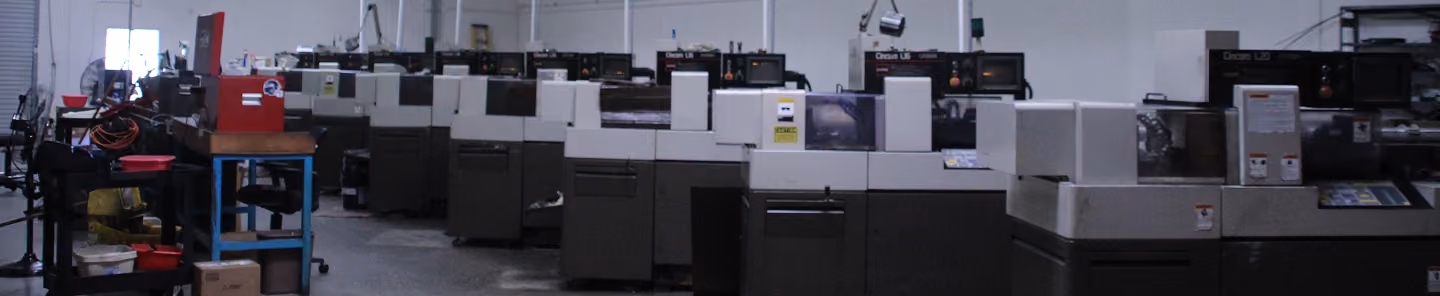 Large row of industrial CNC machines in a spacious, dimly lit factory workshop.