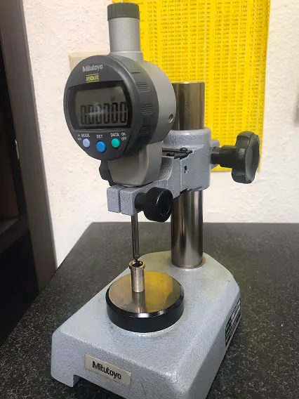 Mitutoyo digital height gauge instrument measuring a small cylindrical metal part on a black surface.