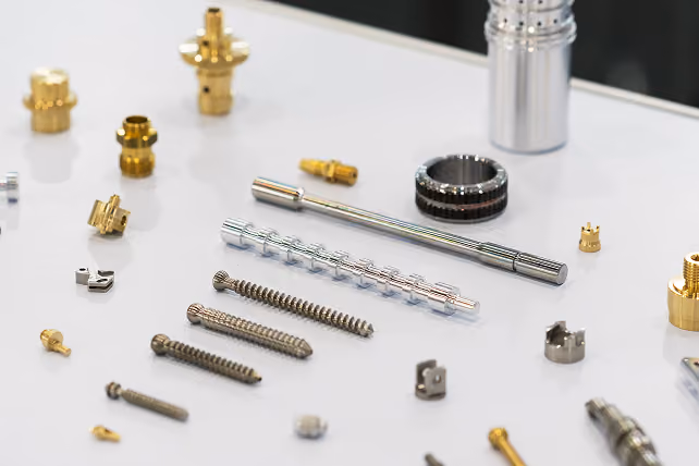 Various small metal mechanical parts and screws arranged on a white surface.