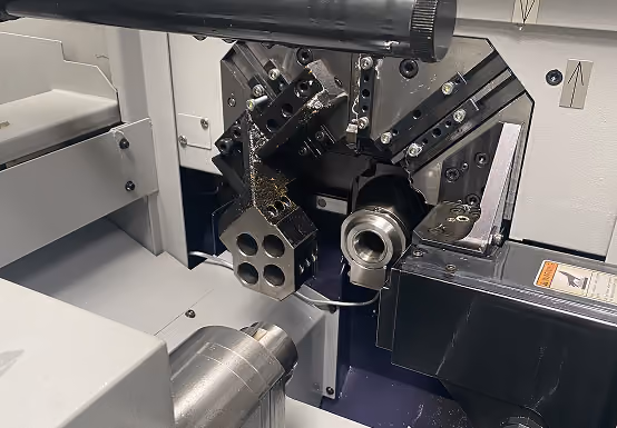 Close-up of a metalworking machine's tool turret and chuck inside a CNC lathe.