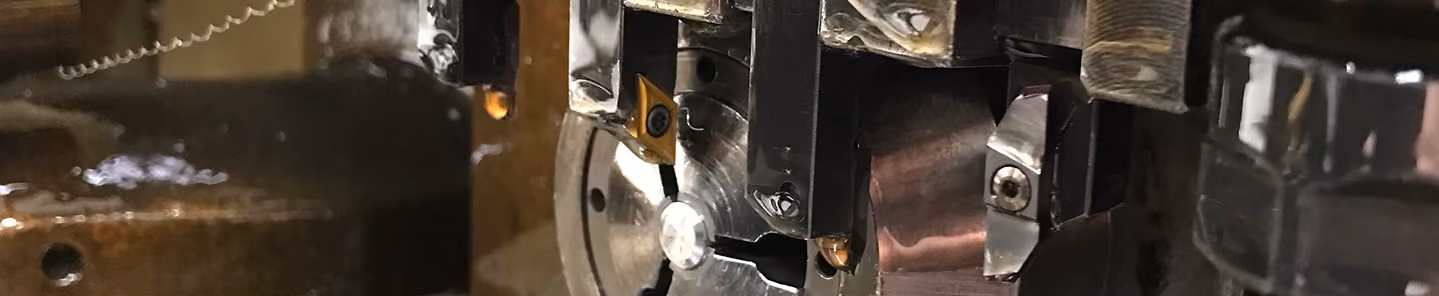 Close-up of a metal lathe machine chuck holding a metal workpiece with cutting tools attached.