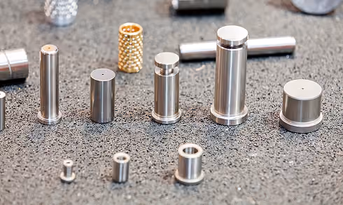 Various small metallic cylindrical components arranged on a textured surface.