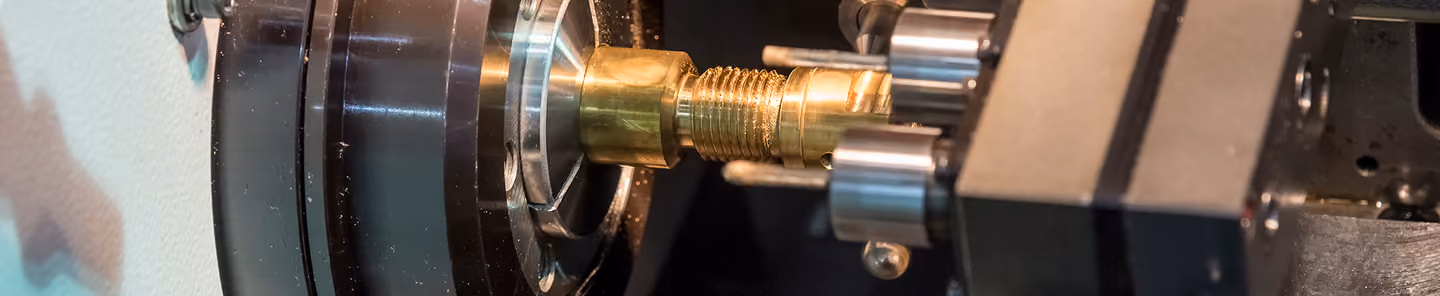 Close-up of a metal lathe machine cutting a threaded screw on a brass workpiece.