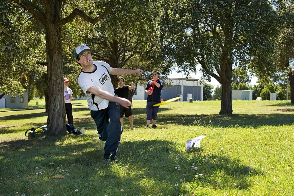 A boy throwing a disc beneath a large tree while other players watch.