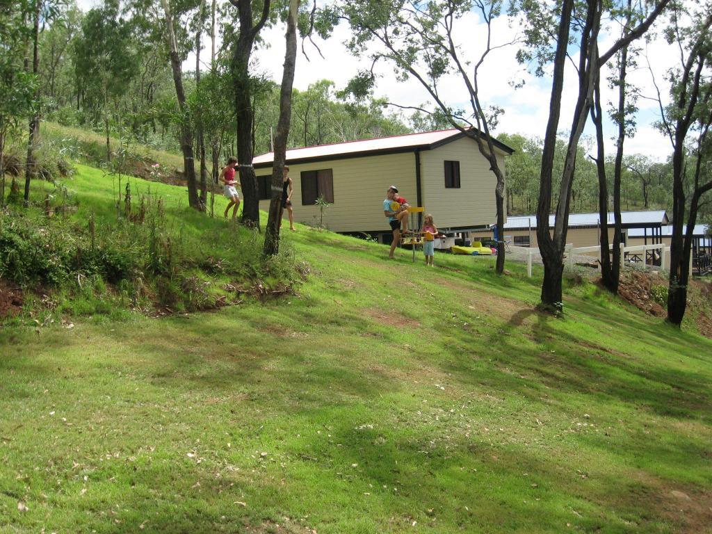 Guests playing disc golf on a grassy hillside at Cania Gorge Caravan & Tourist Park in Queensland, surrounded by cabins, trees and bushland.