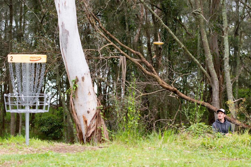 Disc golfer throwing toward a basket on the wooded Rathmines Disc Golf Course at Styles Point Reserve, Lake Macquarie.