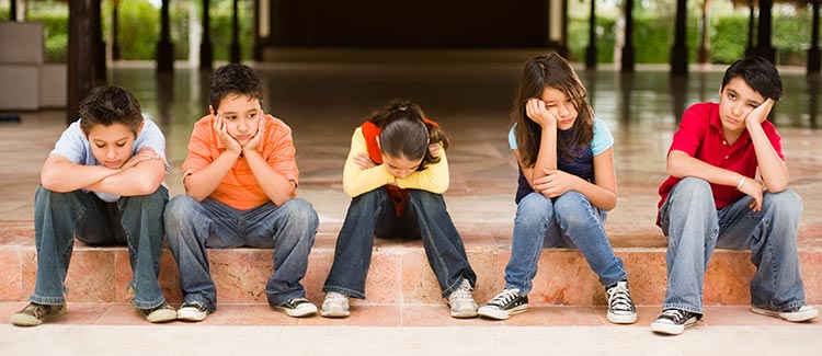 Five bored children sitting in a row on steps with their chins resting on their hands.