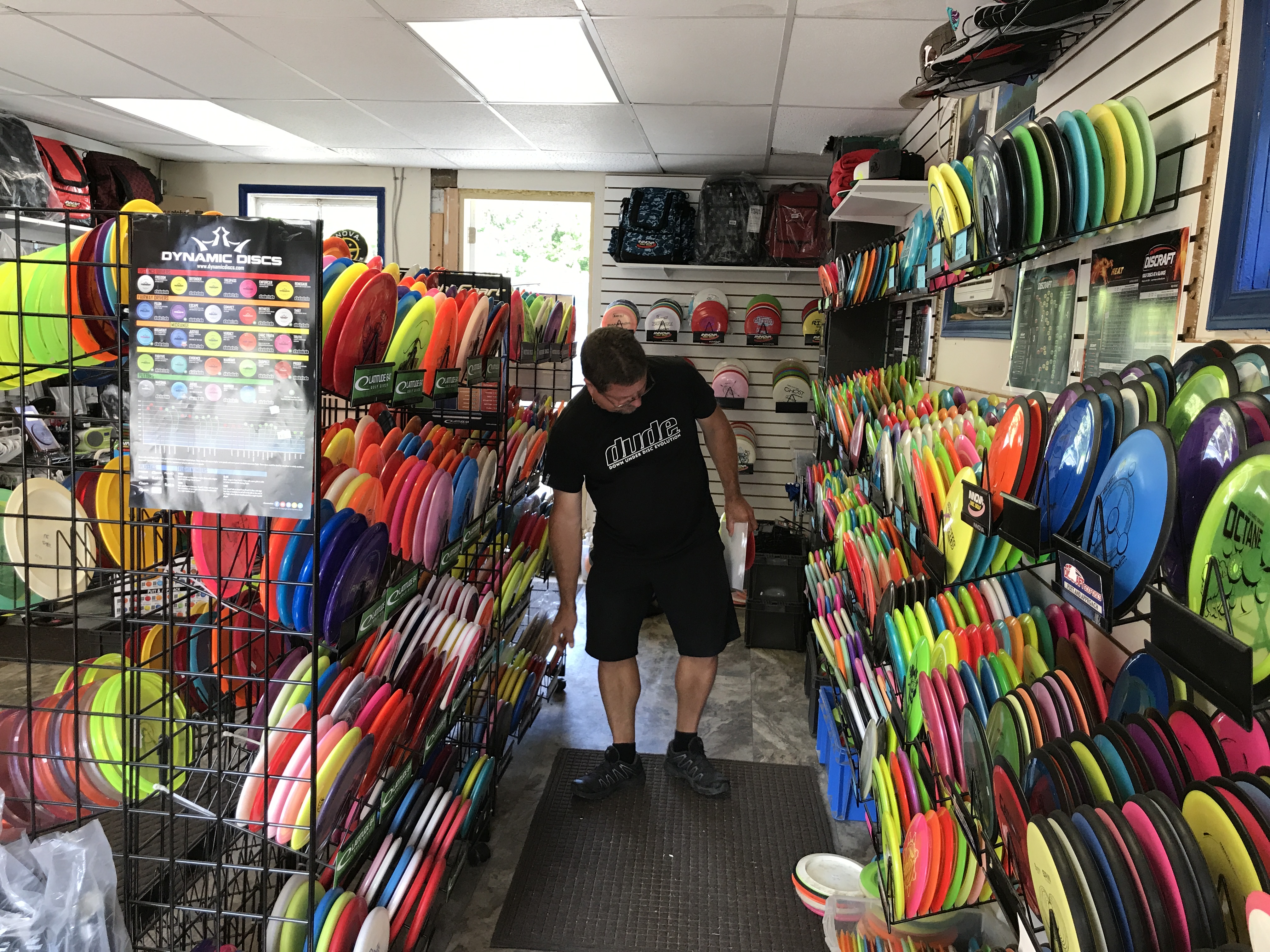 Inside a disc golf shop, a customer browsing walls stacked with coloured discs.