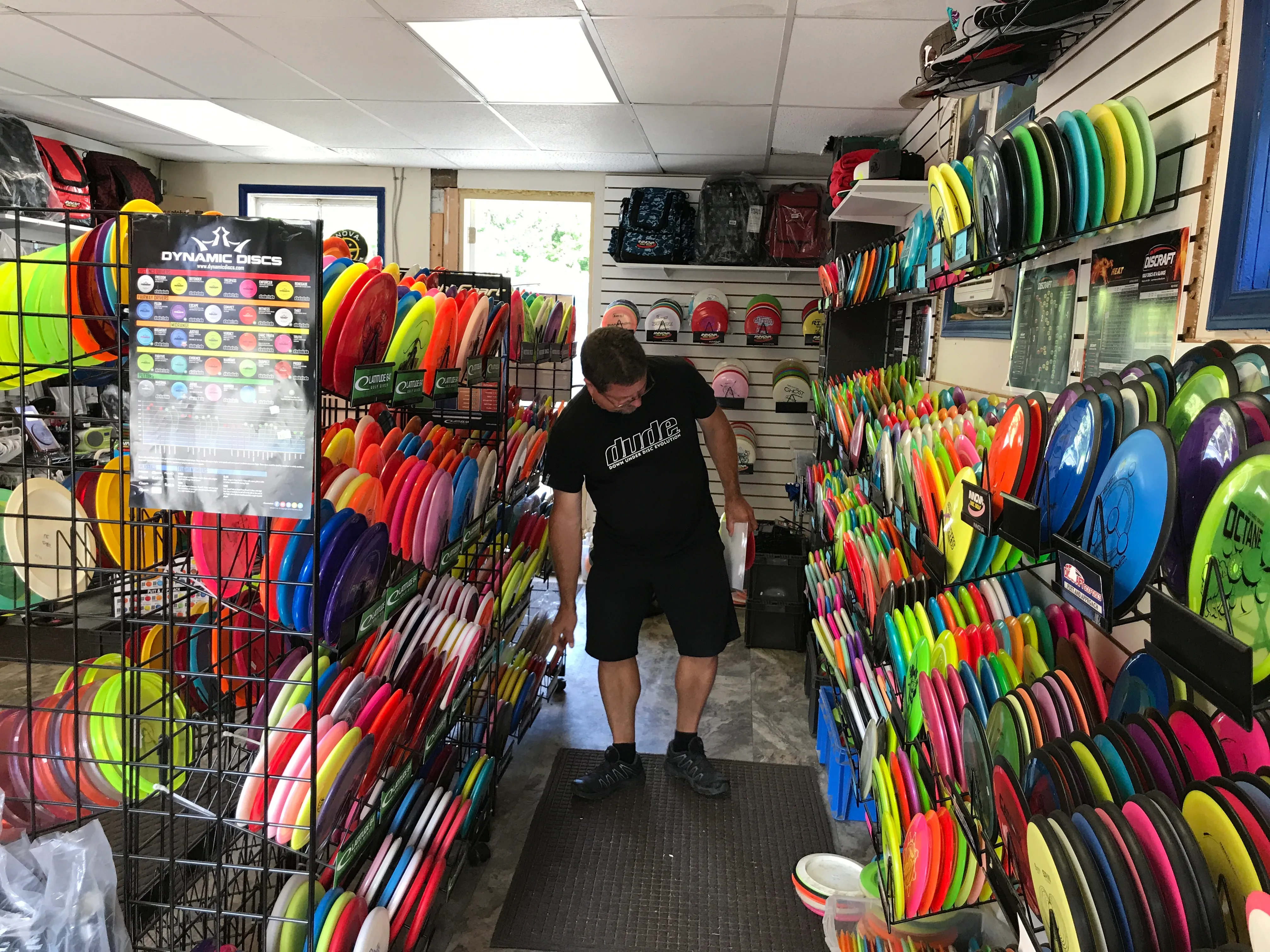 Inside a disc golf shop, a customer browsing walls stacked with coloured discs.