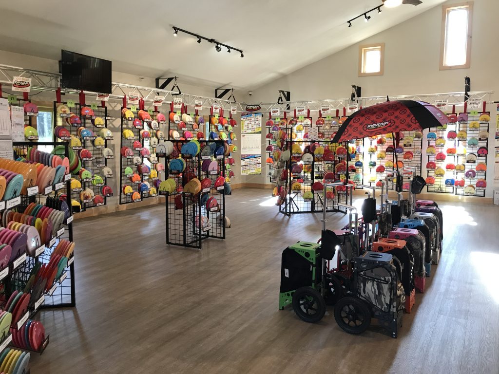 The interior of a disc golf store, with racks of discs lining the walls and bags displayed on the floor.