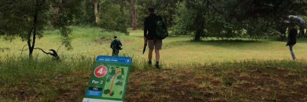 Players walking an open grassy fairway past a numbered tee sign on a lightly wooded course.