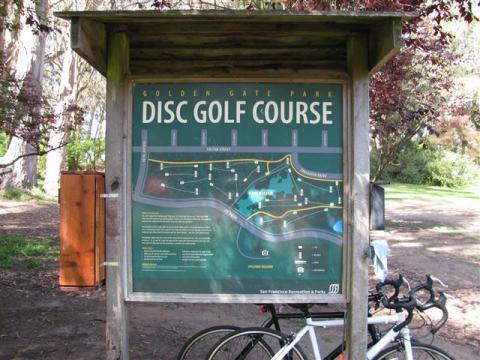 A timber information board showing the Golden Gate Park disc golf course map, with a bicycle leaning against it.