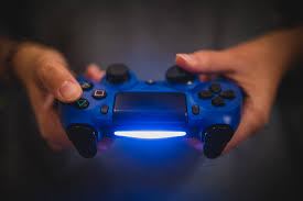 Hands holding a glowing blue games console controller in a darkened room.