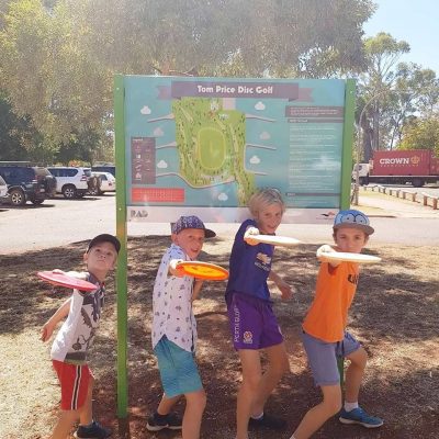 Four boys holding discs and posing in front of the Tom Price Disc Golf information board.