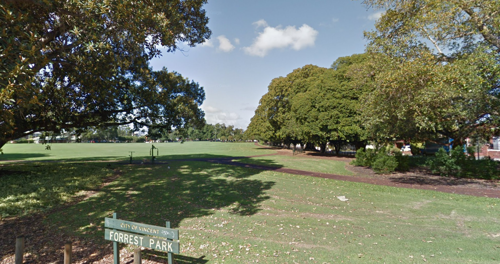 Open parkland with mature trees and mown grass, a Forrest Park sign at the edge.