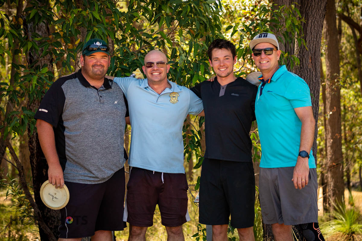 Four players posing together with discs in front of bushland at a tournament.