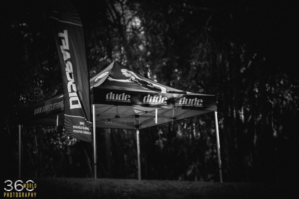 A black and white photograph of a Dude Clothing branded event marquee at a tournament.
